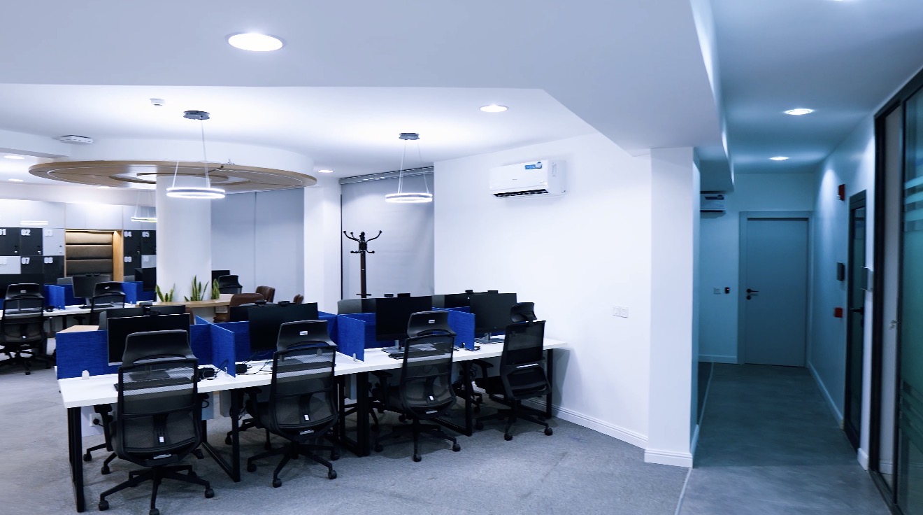 Roche Abuja open workplace with bench workstations, blue desk screens and a corridor to glazed meeting rooms.