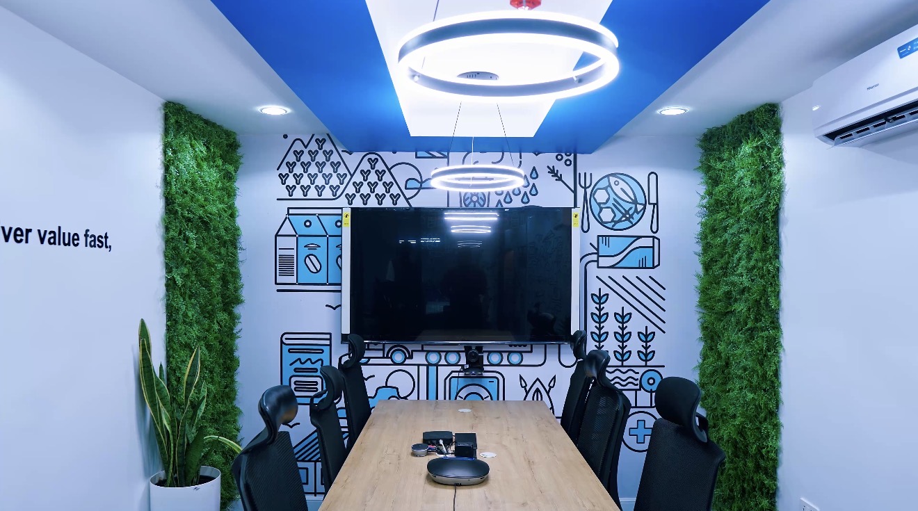 Roche Abuja collaboration room with timber table, display screen, illustrated wall graphic and green wall panels.