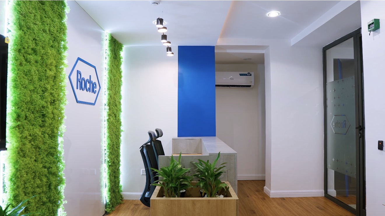 Roche Abuja reception with an illuminated green brand wall, timber desk and glazed entrance.