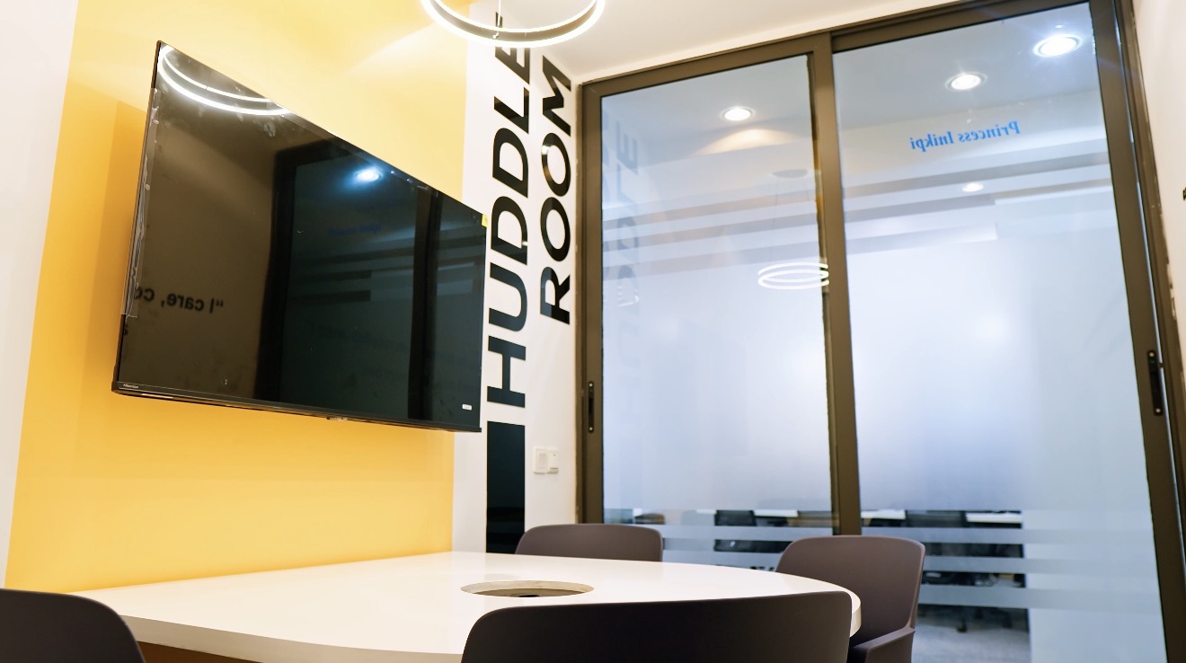 Roche Abuja huddle room with a yellow feature wall, display screen, white table and glazed enclosure.