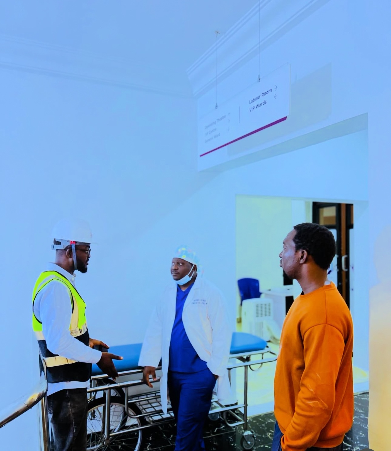 Site discussion in a hospital circulation area beneath wayfinding signage.