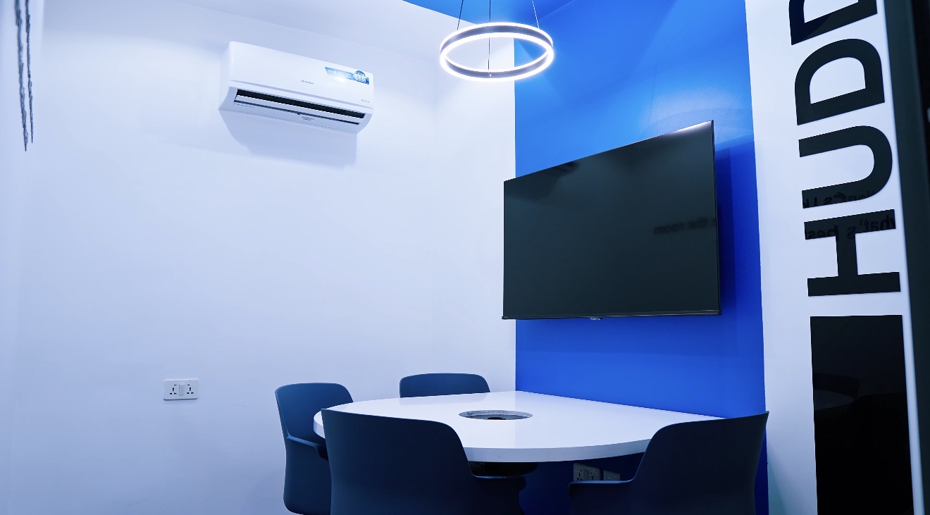Roche Abuja huddle room with a blue feature wall, display screen, circular light and compact meeting table.