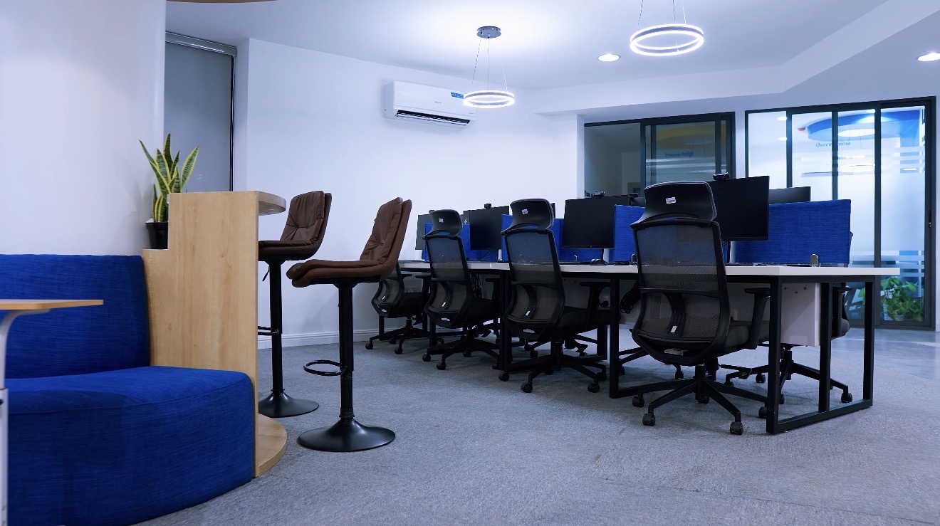 Roche Abuja open workplace with blue banquette seating, workstations, monitors and glazed meeting rooms.