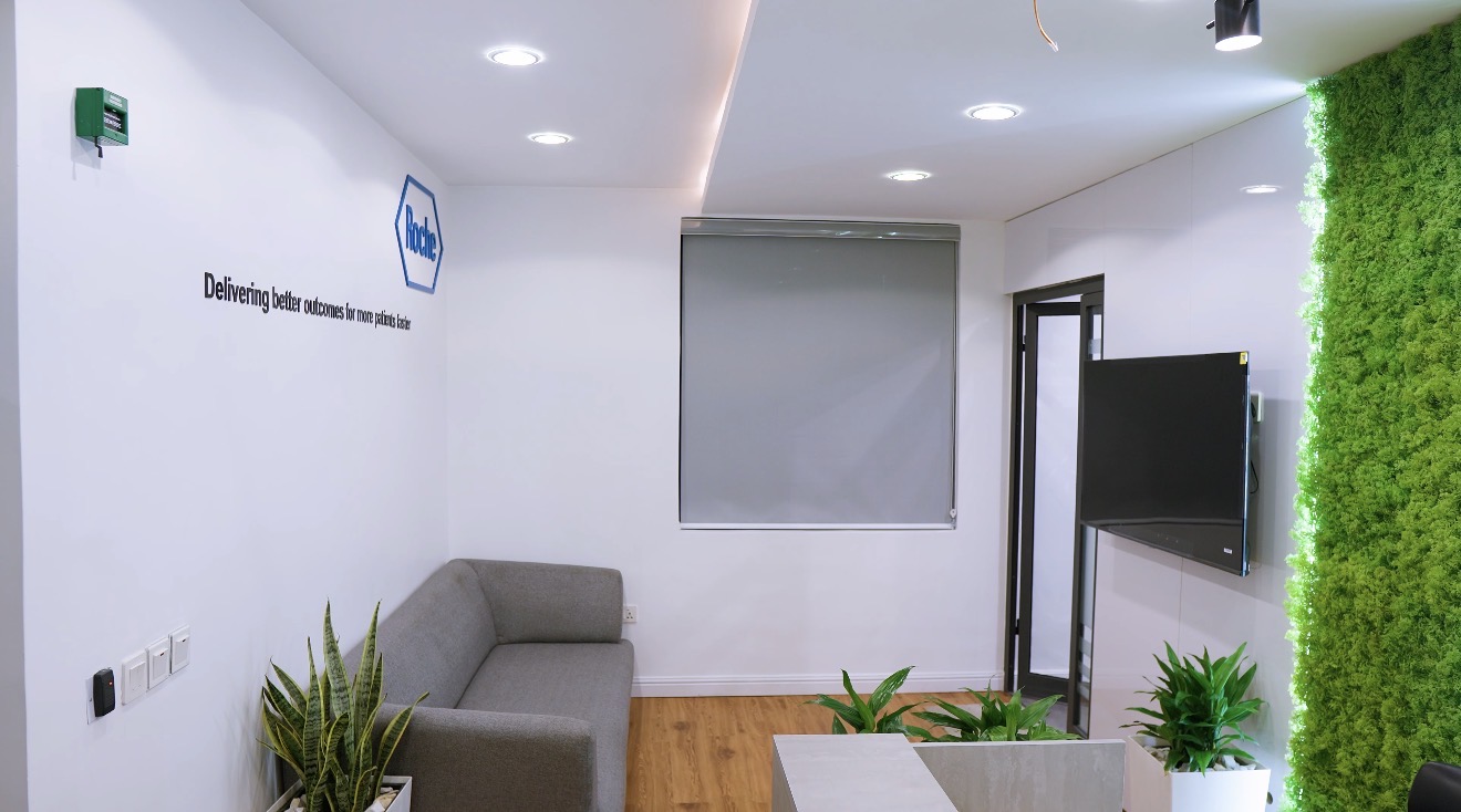 Roche Abuja reception lounge with grey seating, integrated planting, display screen and illuminated green wall.