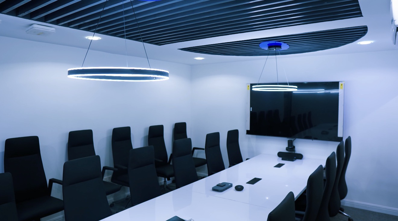 Roche Abuja meeting room with a long white table, display screen, black seating and linear ceiling detail.