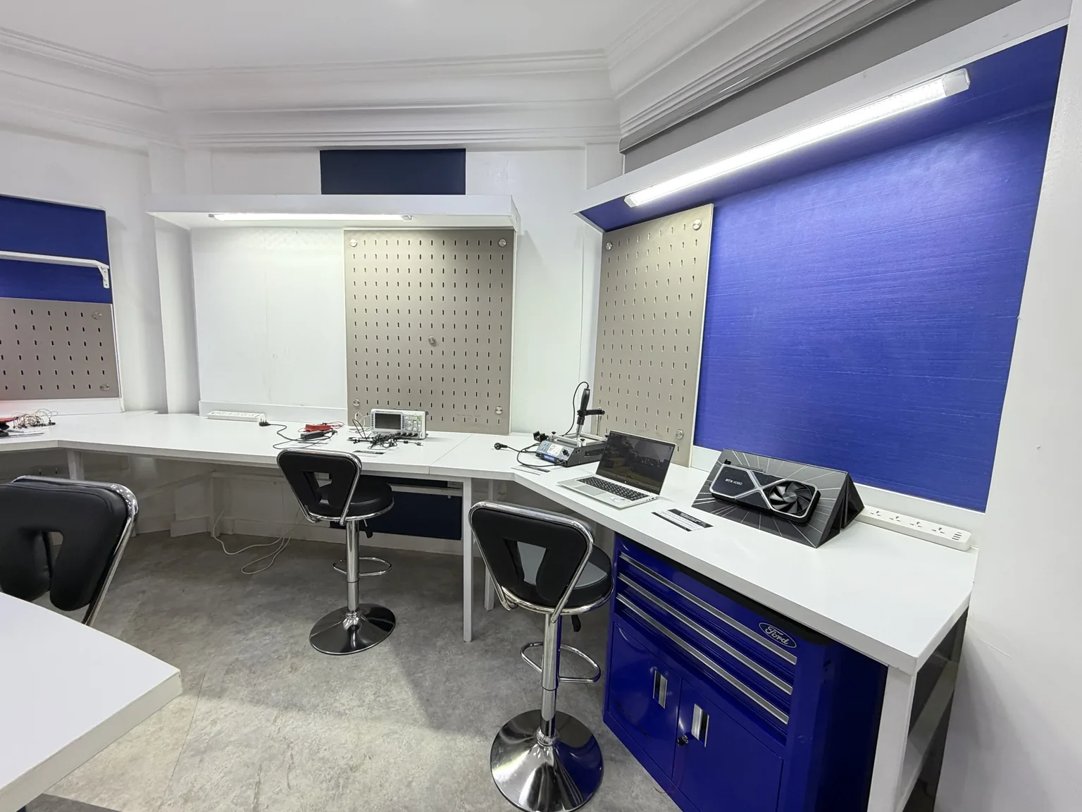 Electronics workbench in the Miva robotics lab, with task lighting and tool storage above.