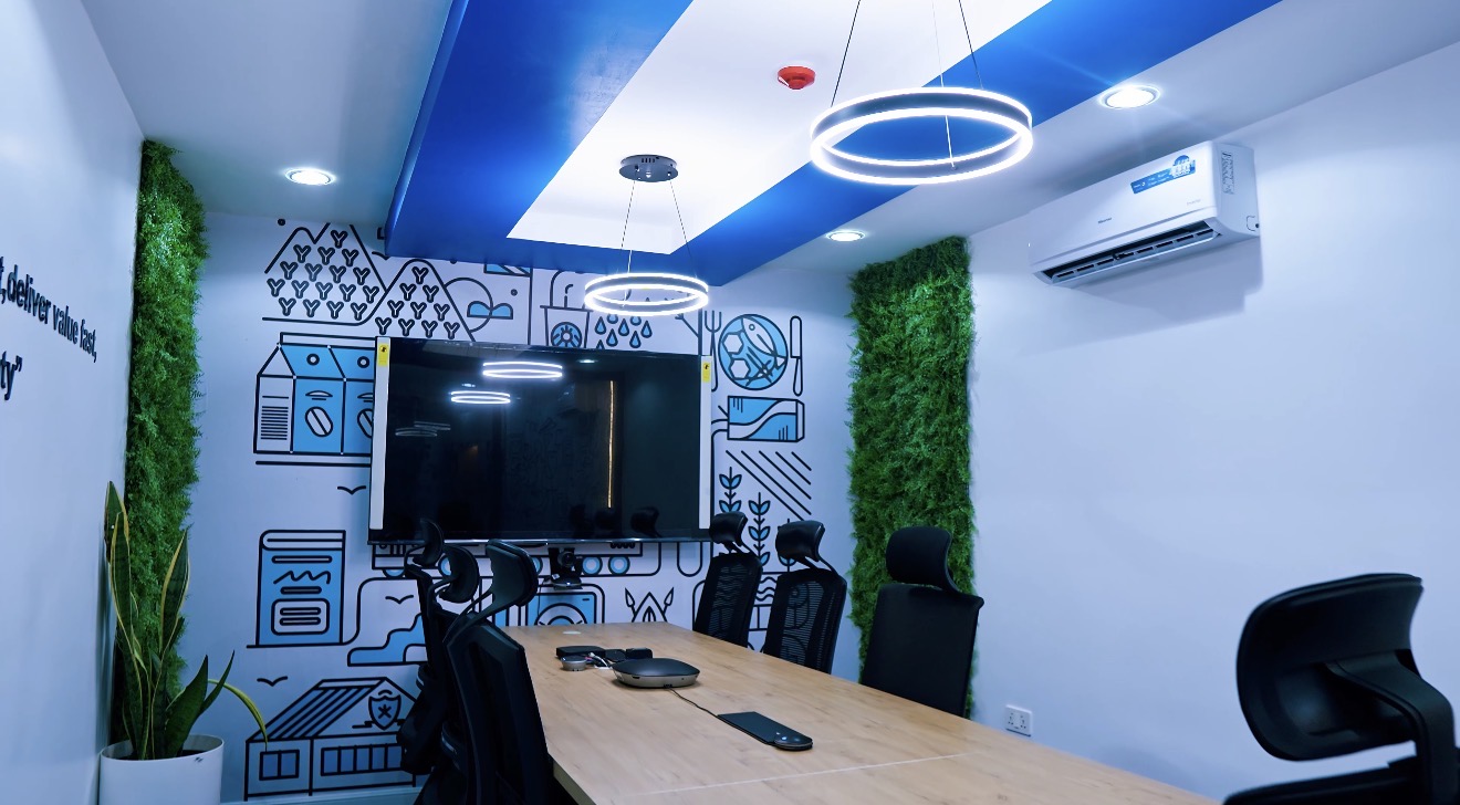 Roche Abuja collaboration room with timber meeting table, illustrated wall graphic, green wall panels and circular pendant lights.